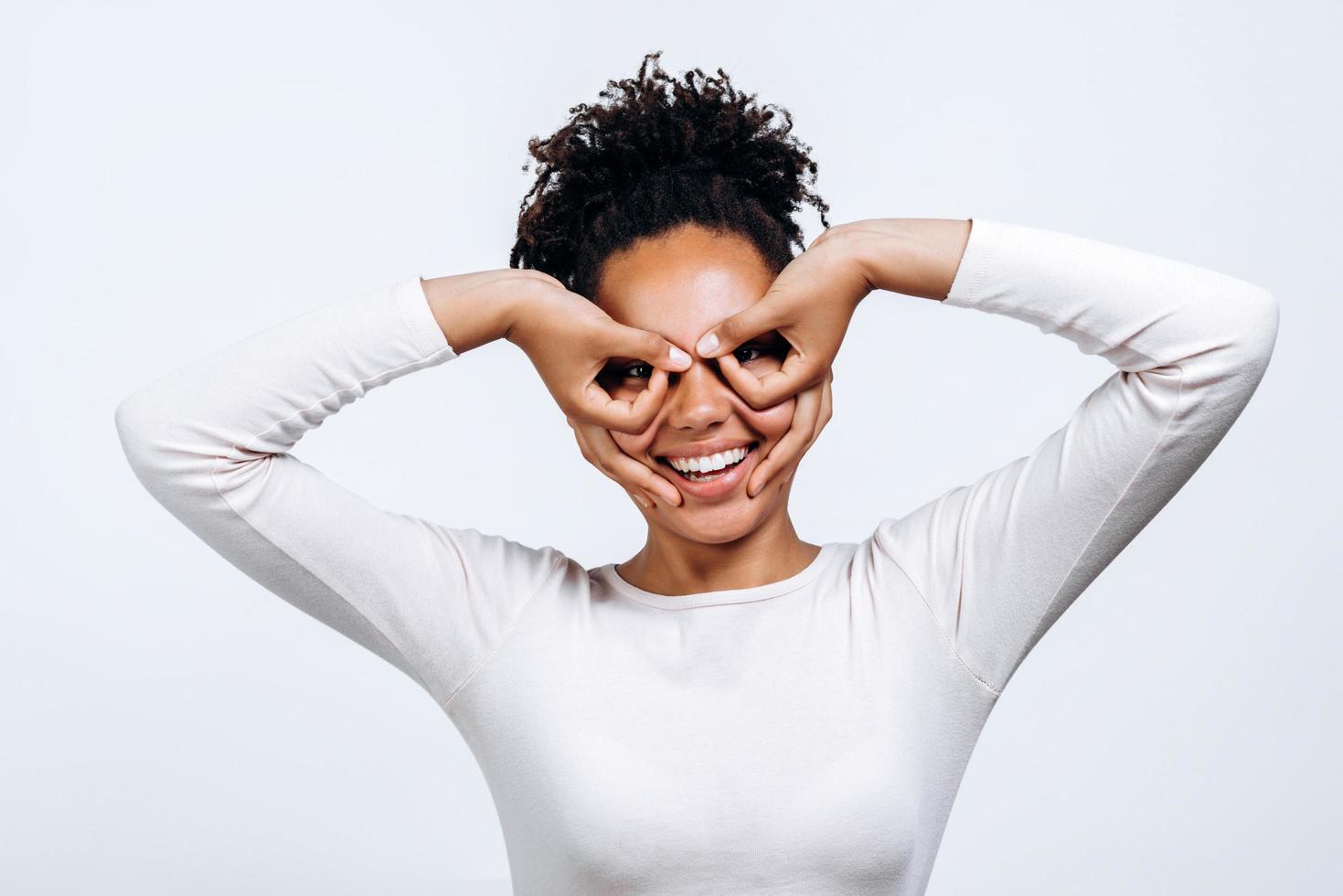 Portrait of a positive and emotional beautiful young woman, made from fingers a figure similar to the pilot glasses around her eyes isolated on a white wall. photo