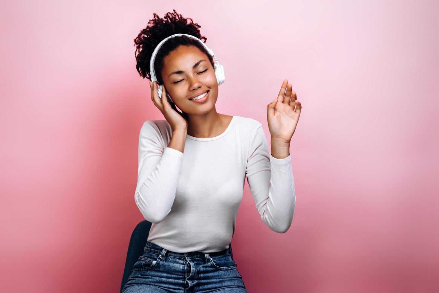 hermosa y linda chica en auriculares escucha música sobre un fondo de una pared rosa foto