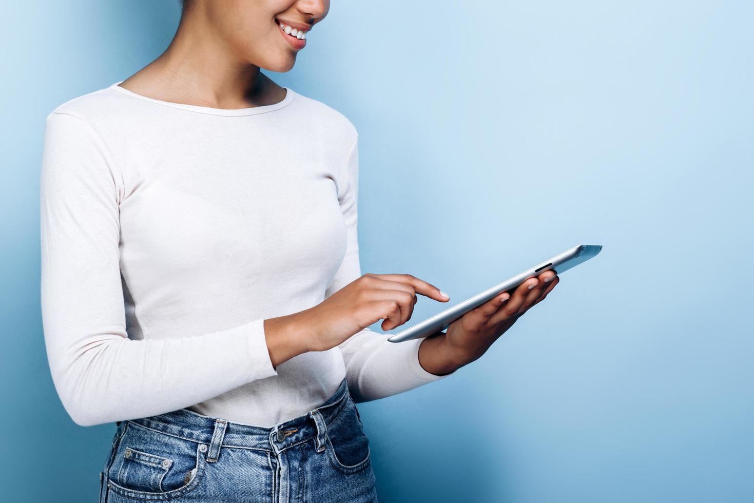 Close up, side view of a girl working with a tablet on a background of blue wall photo