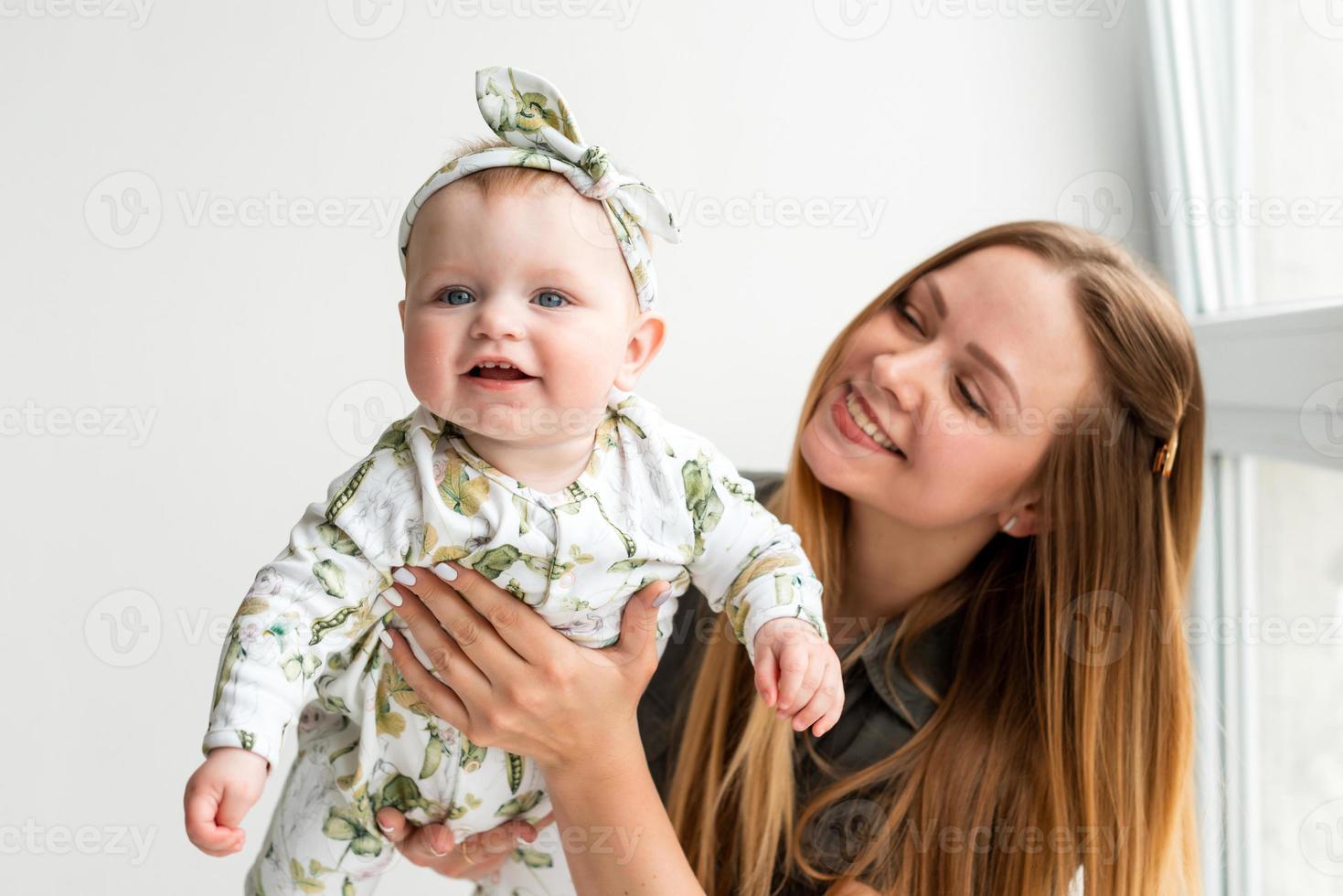 Linda y sonriente madre sosteniendo a su pequeña hija en sus brazos, divirtiéndose foto