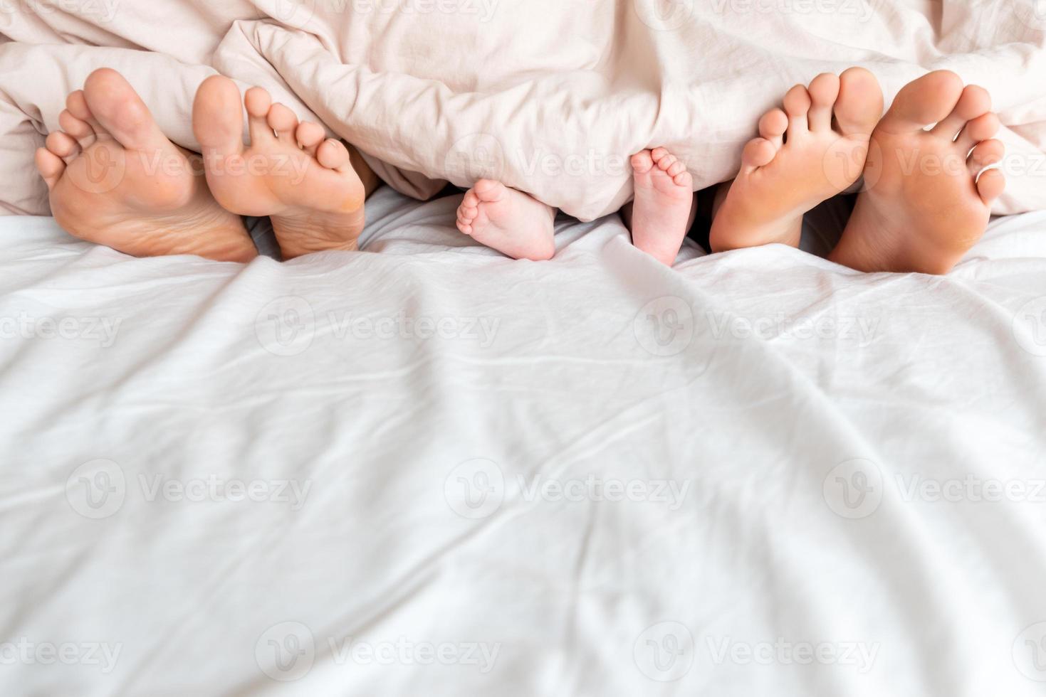 The legs of a child, mom and dad peek out from under the white blanket photo