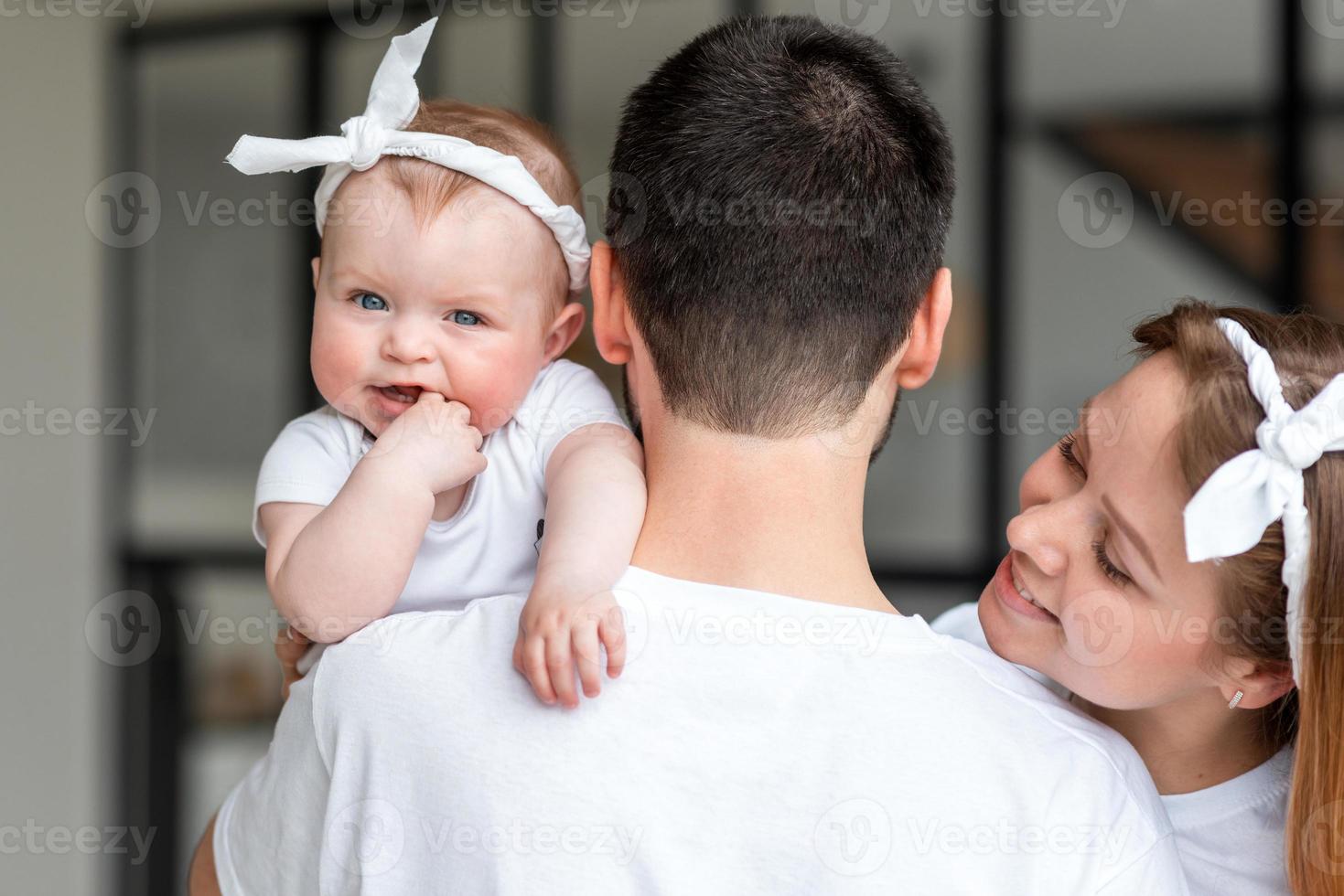 Rear view, father holding little daughter in his arms, smiling wife sincerely happy. photo