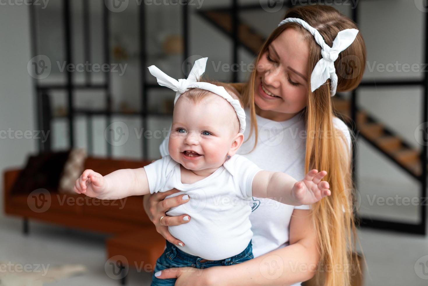 Feliz y sonriente mujer sosteniendo a una pequeña y hermosa hija en sus brazos en el apartamento foto