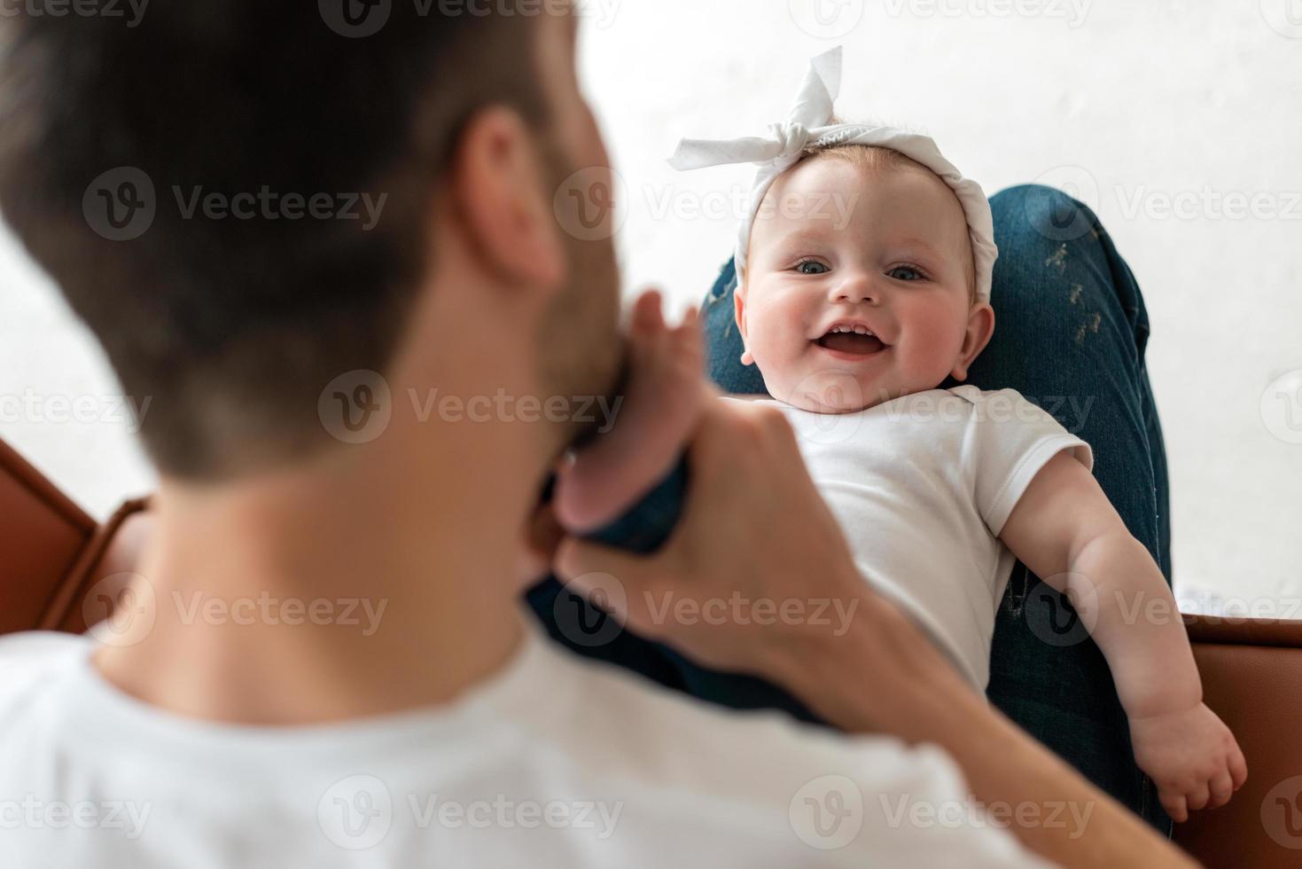 lindo y cariñoso papá besa las piernas pequeñas y tiernas de su hermosa y pequeña hija foto