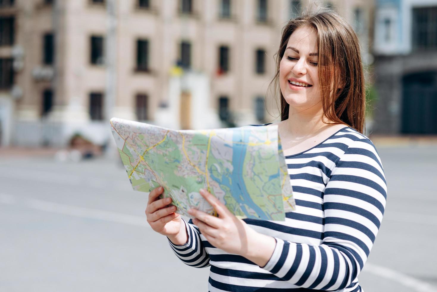 Mujer joven alegre con mapa turístico en las manos disfrutando de un hermoso paseo durante su viaje de primavera, mujer feliz con linda sonrisa estudiando atlas antes de caminar en una ciudad extranjera durante el viaje de verano foto