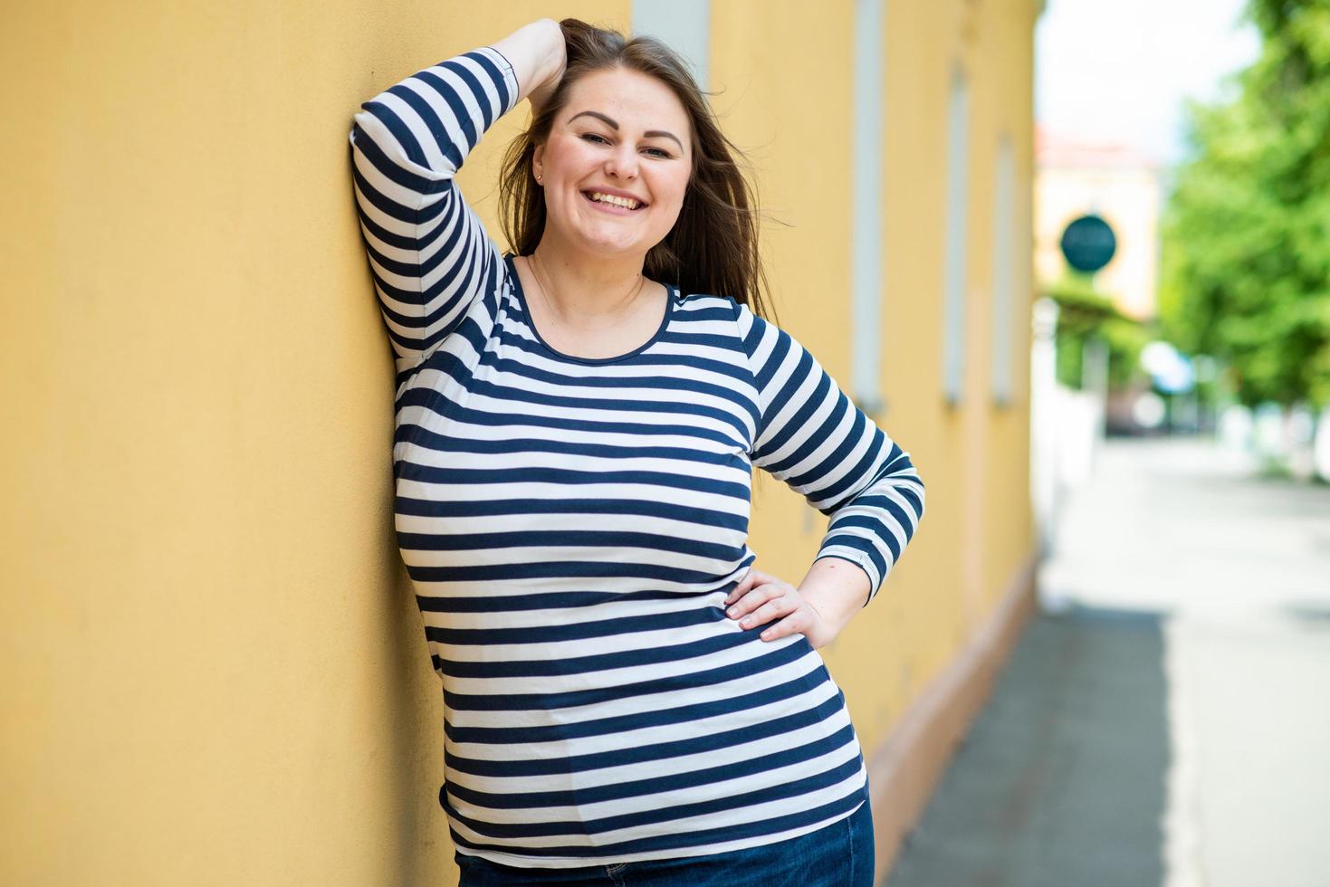 Sonriente mujer alegre plus size posando al aire libre sobre fondo de pared naranja foto