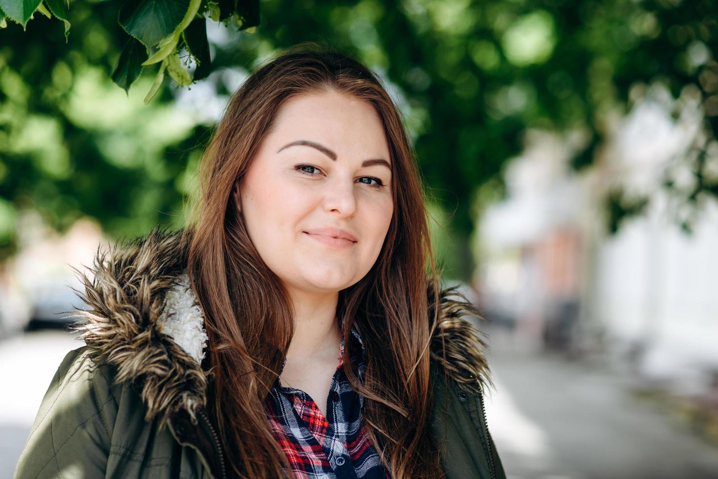 Attractive, pretty woman looking straight into the camera outdoors under a green tree photo