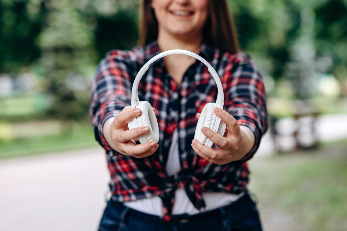 Mujer plus size en camiseta colorida sosteniendo auriculares inalámbricos, al aire libre foto