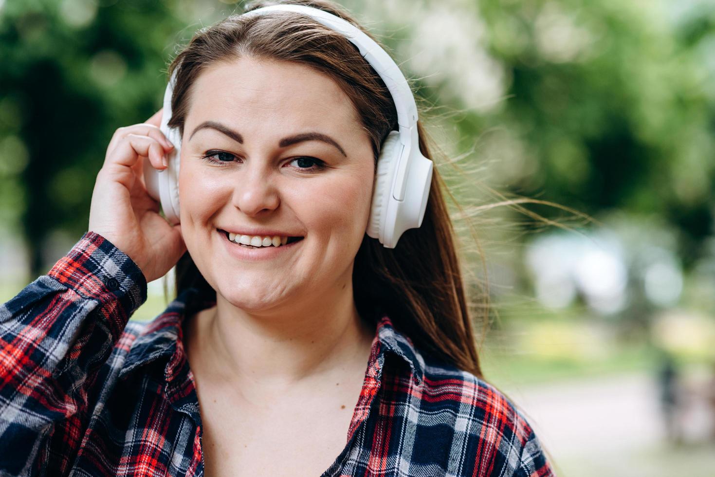 Young woman wearing headphones with a happy face standing in the middle of the park photo