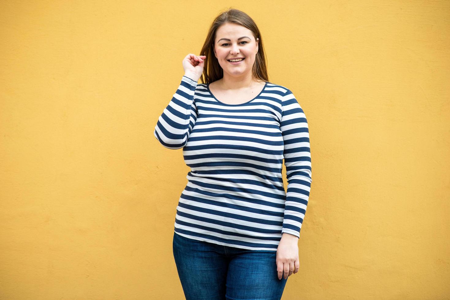 Overweight woman in a striped sweater posing on the background of an orange wall photo