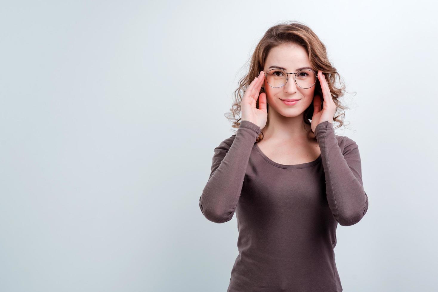 Girl trying new glasses. Portrait of satisfied good looking female customer, wearing stylish transparent eyewear and smiling over gray background. photo