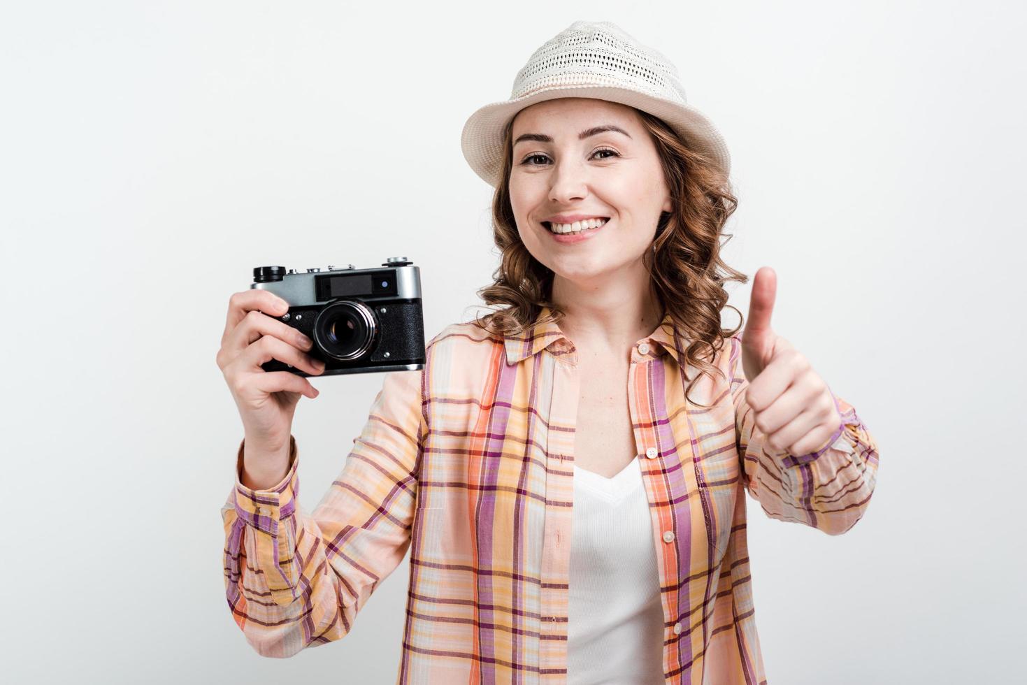 chica guapa con sombrero y retrocamera en manos está satisfecha con su trabajo, mostrando el pulgar hacia arriba. foto