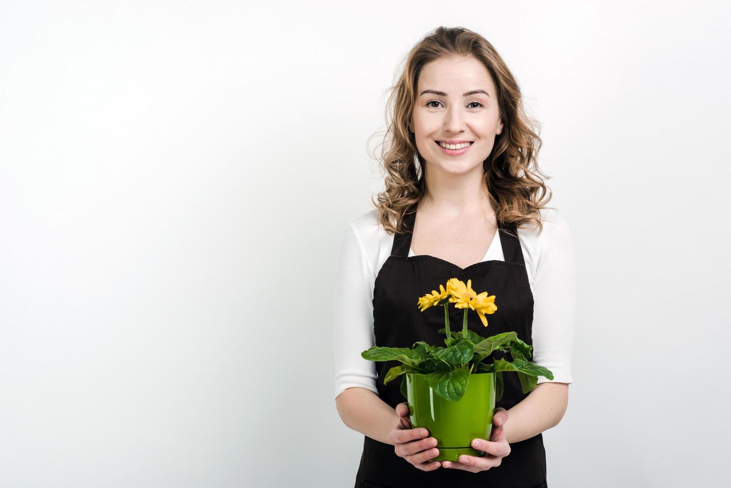 Beautiful, smiling girl holds a flowerpot in her hands, posing in studio on a white wall background photo