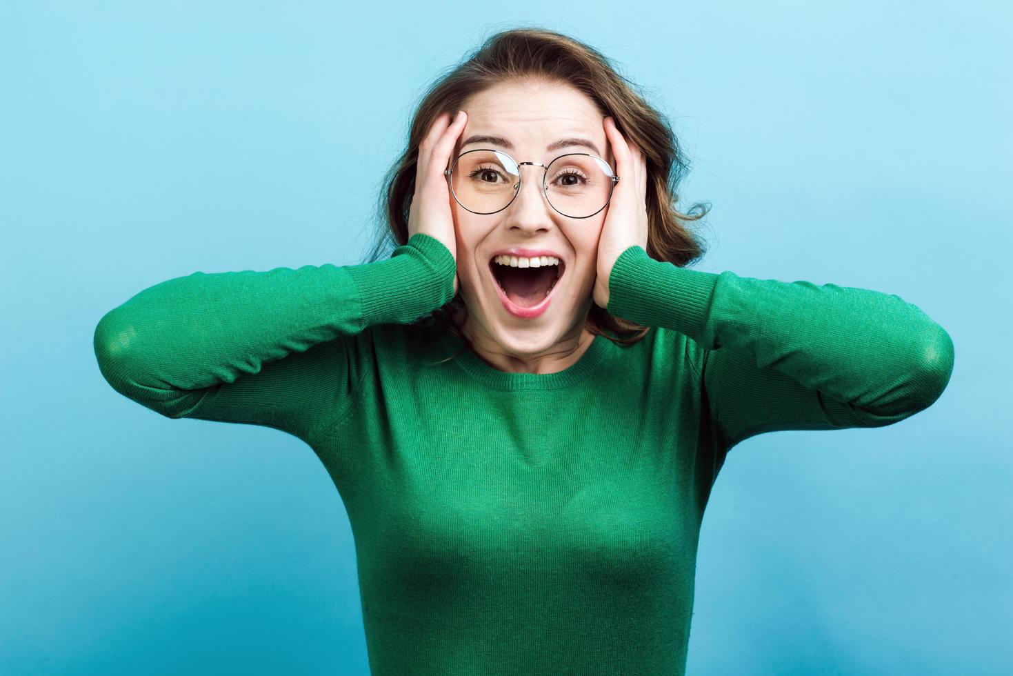 Girl in panic holds hands behind her head, against a blue background. photo