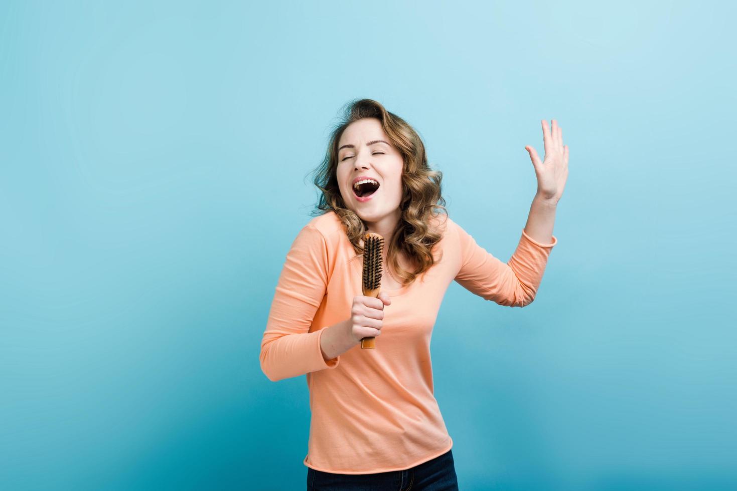 Cheerful girl with hair brush sings. On a blue background. photo