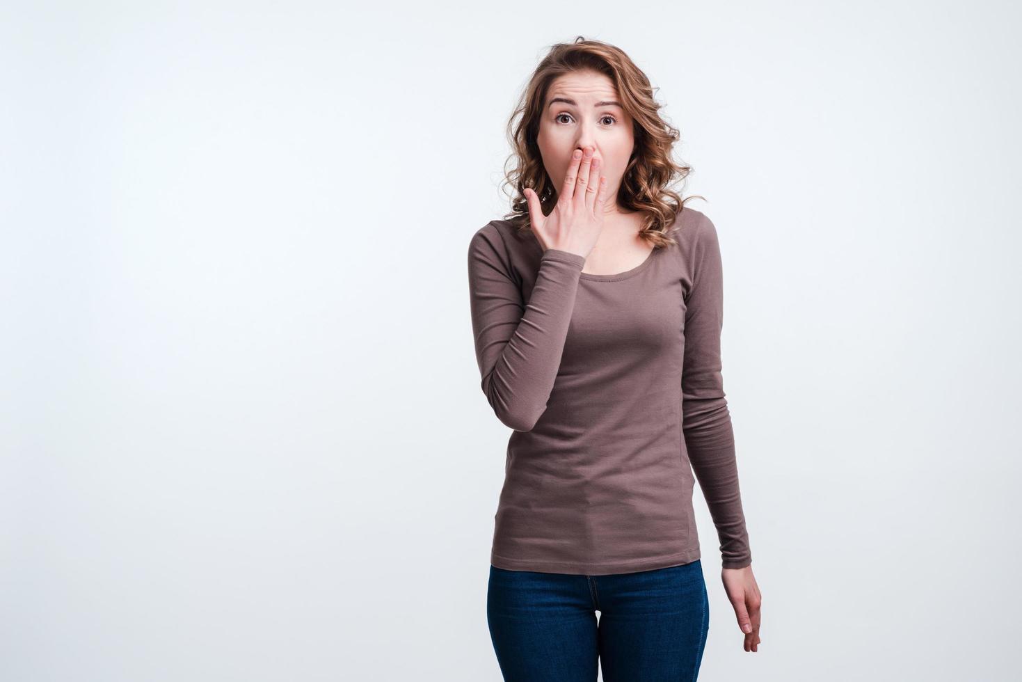 Excited girl covers his mouth with his hand on white wall background in studio photo