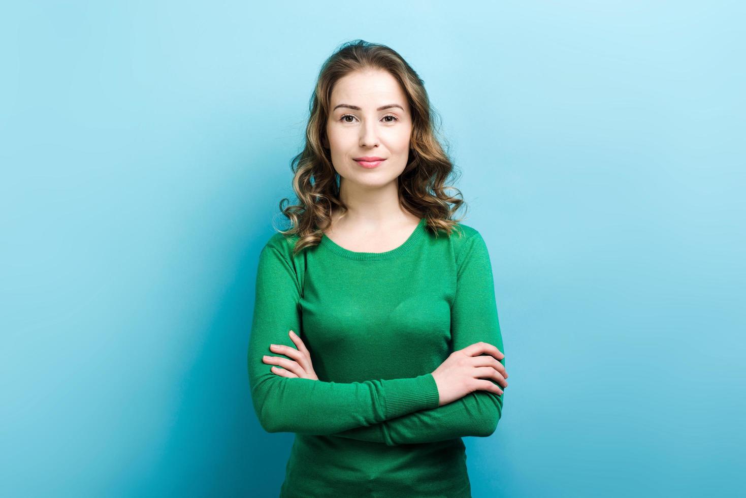 Pretty, young woman with crossed arms on blue wall background photo