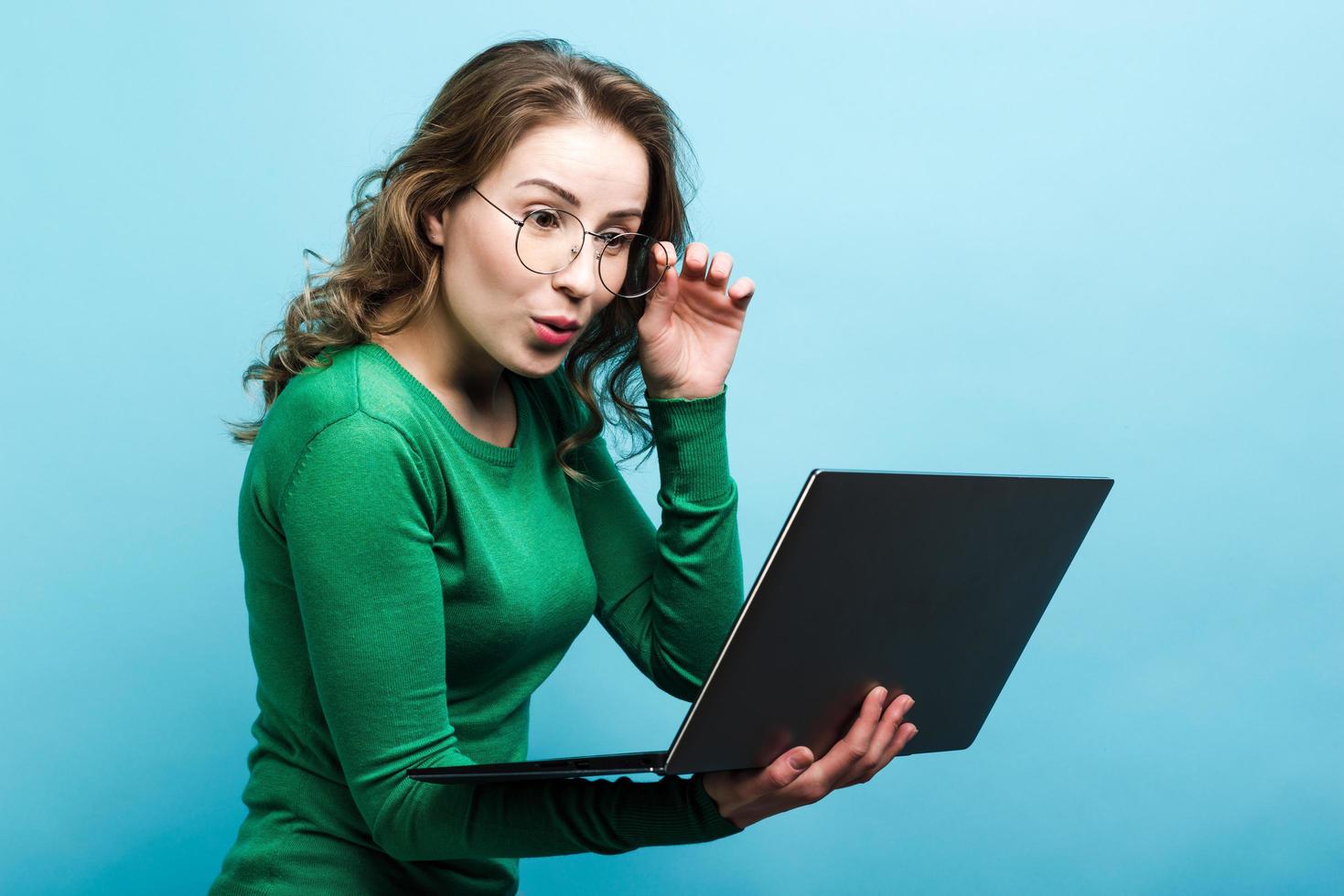 Girl surprised looking at laptop, isolated on blue background. photo