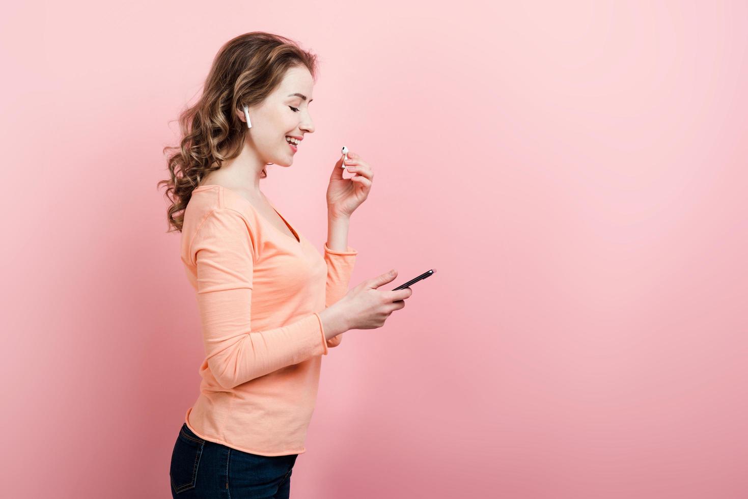 Happy girl in earphones holding   a smarphone in her hand  and looking at the screen photo