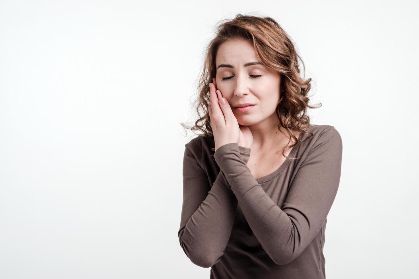 Beautiful young woman suffering from terrible strong teeth pain, touching cheek with hand and closed her eyes. photo