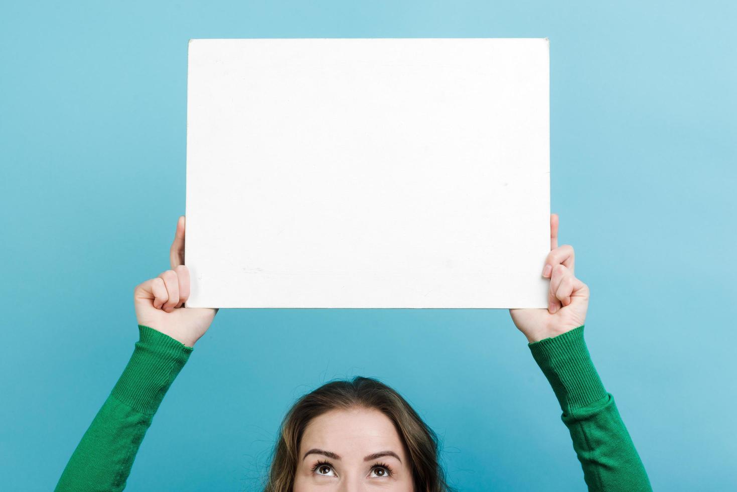 Closeup girl holding a white board copy space above her head against blue background photo