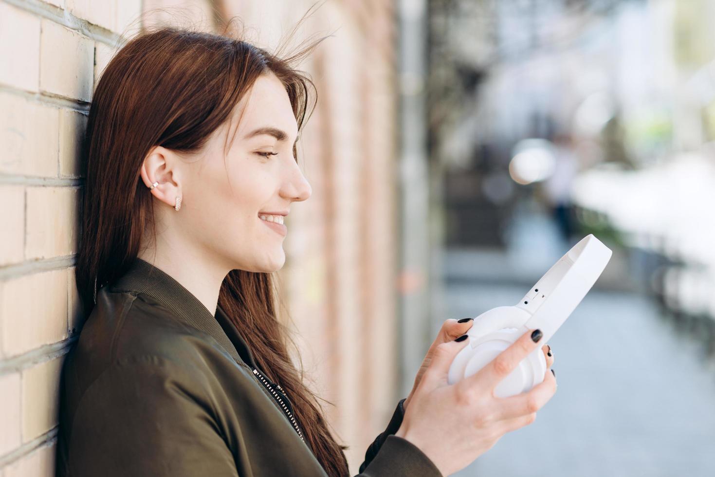 The girl is leaning against a brick wall, wearing headphones photo