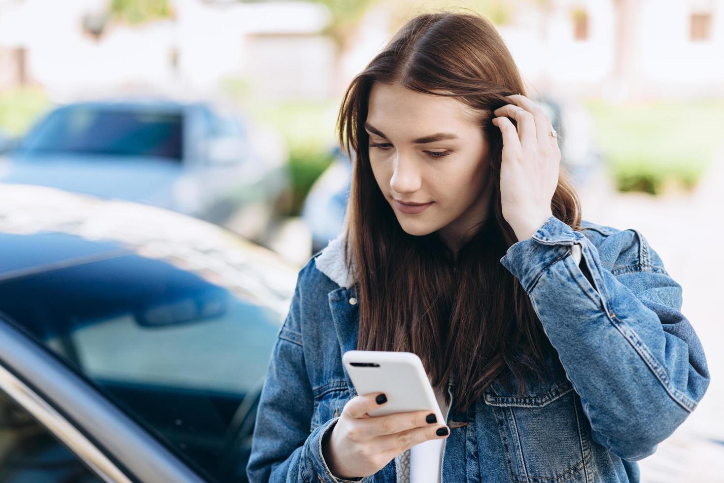 chica interesada enderezar su cabello, mirando algo en un teléfono inteligente en la calle. foto