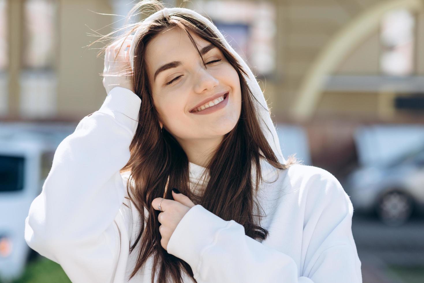 A smiling, enchanted girl in a hood, sincerely rejoices in the open air, city background photo