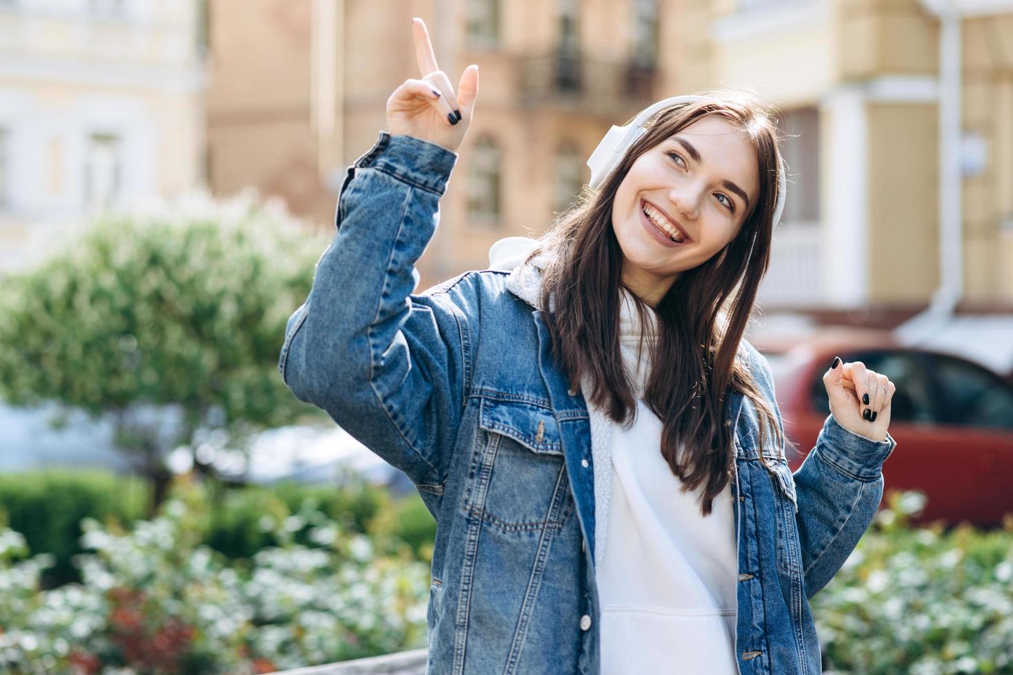 una joven morena elegantemente vestida con antiguos auriculares escucha su música favorita, bailes, con el telón de fondo de la ciudad. foto