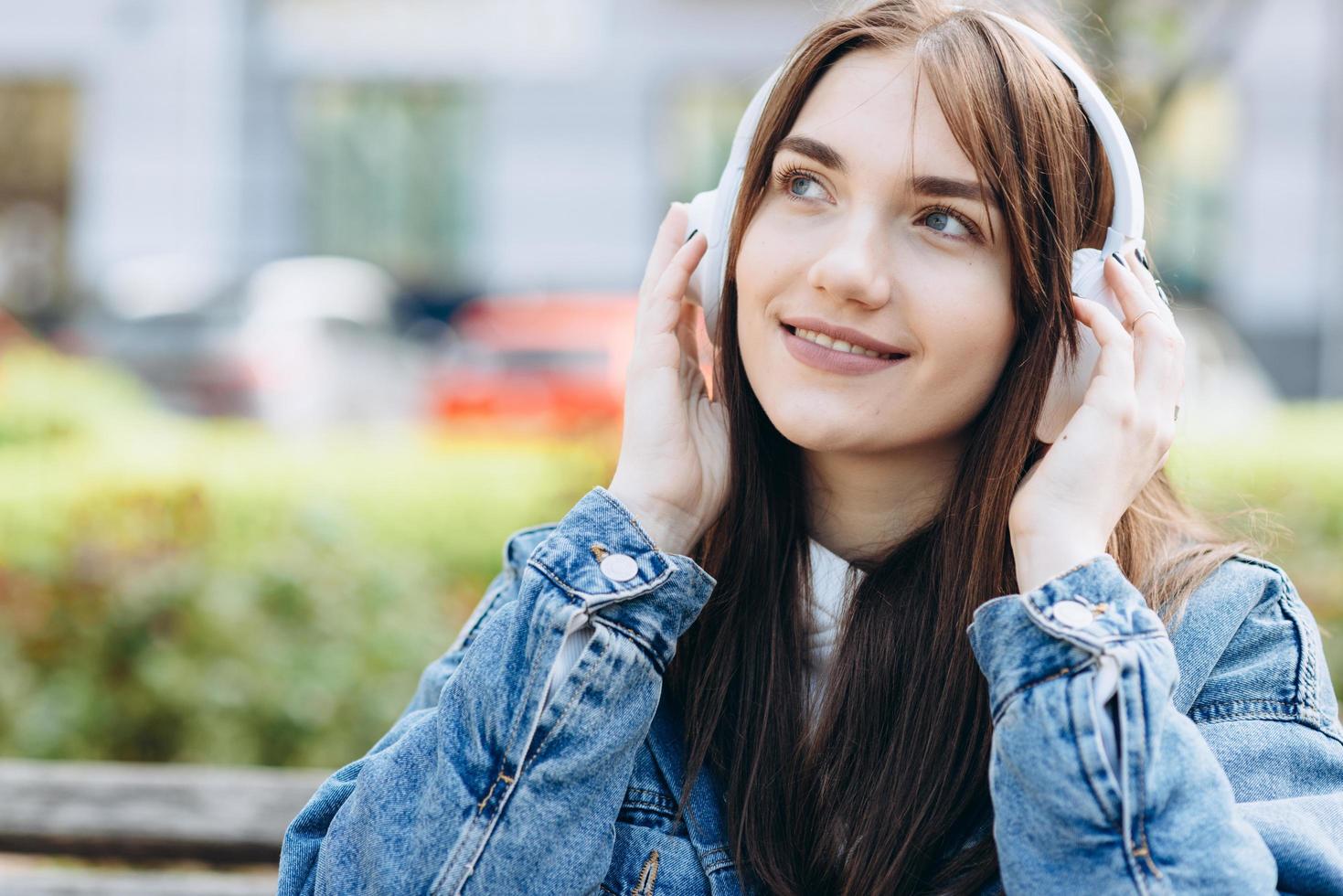 Attractive, young woman, against the backdrop of the city, listening to music, looking at something, enjoying music photo