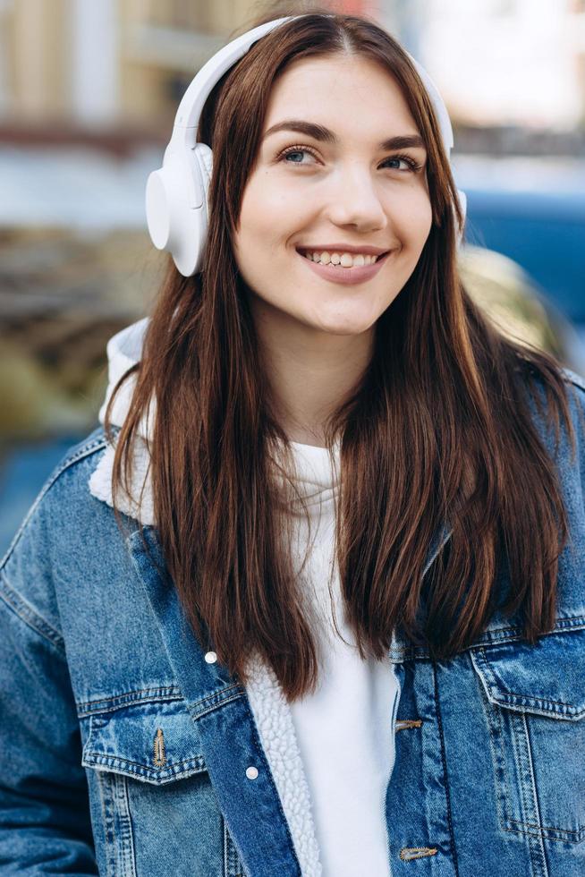 bonita morena con auriculares blancos sonríe coquetamente y disfruta de su música favorita foto