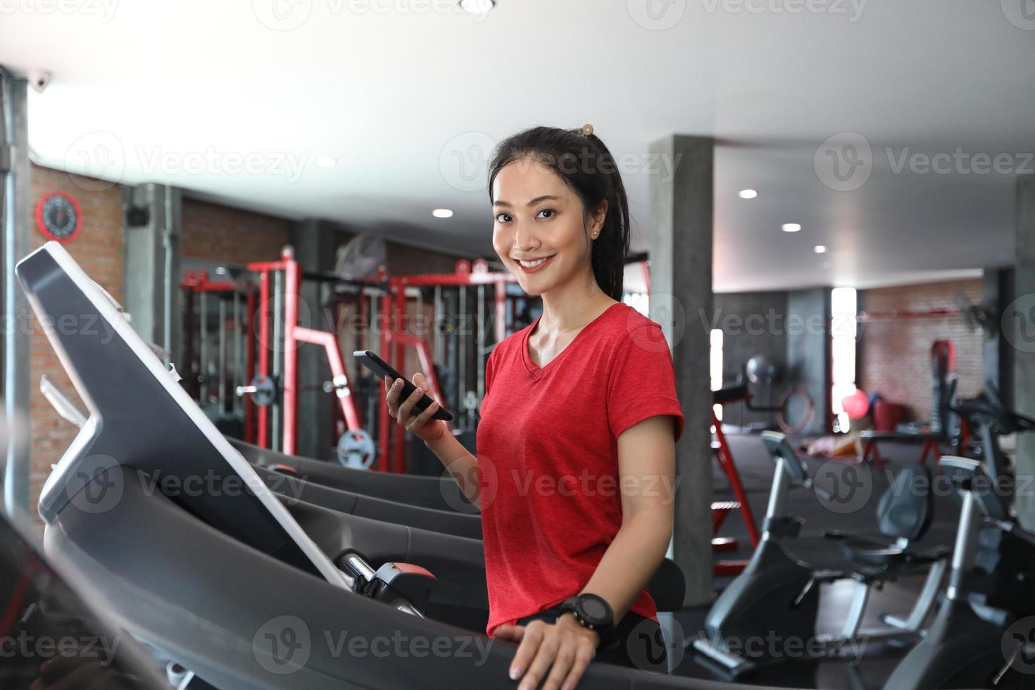 Las mujeres asiáticas corriendo zapatos deportivos en el gimnasio, mientras que una joven mujer caucásica está haciendo jogging en la cinta de correr foto