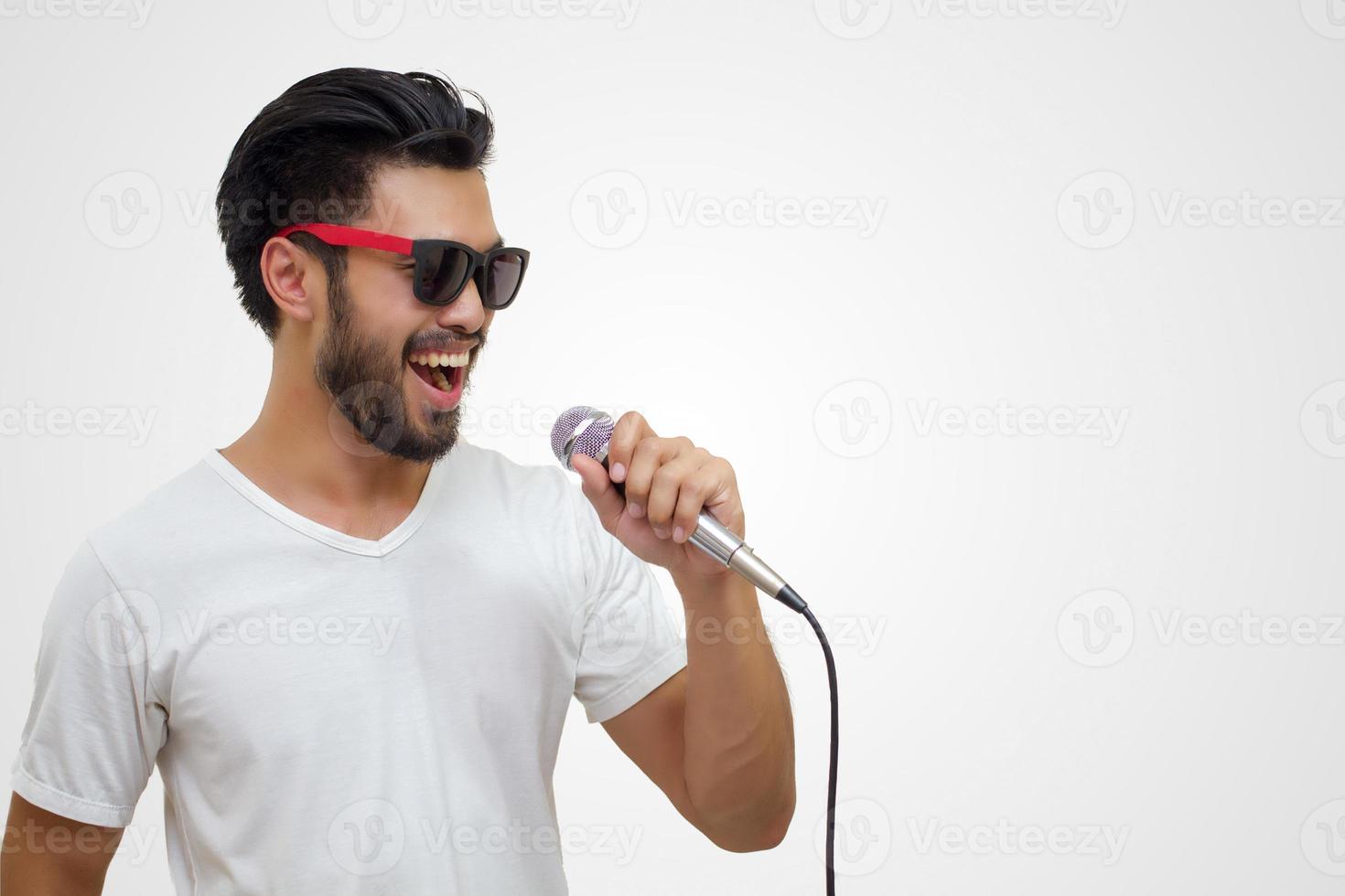 Hombre guapo asiático con bigote, sonriendo y cantando al micrófono aislado sobre fondo blanco. foto