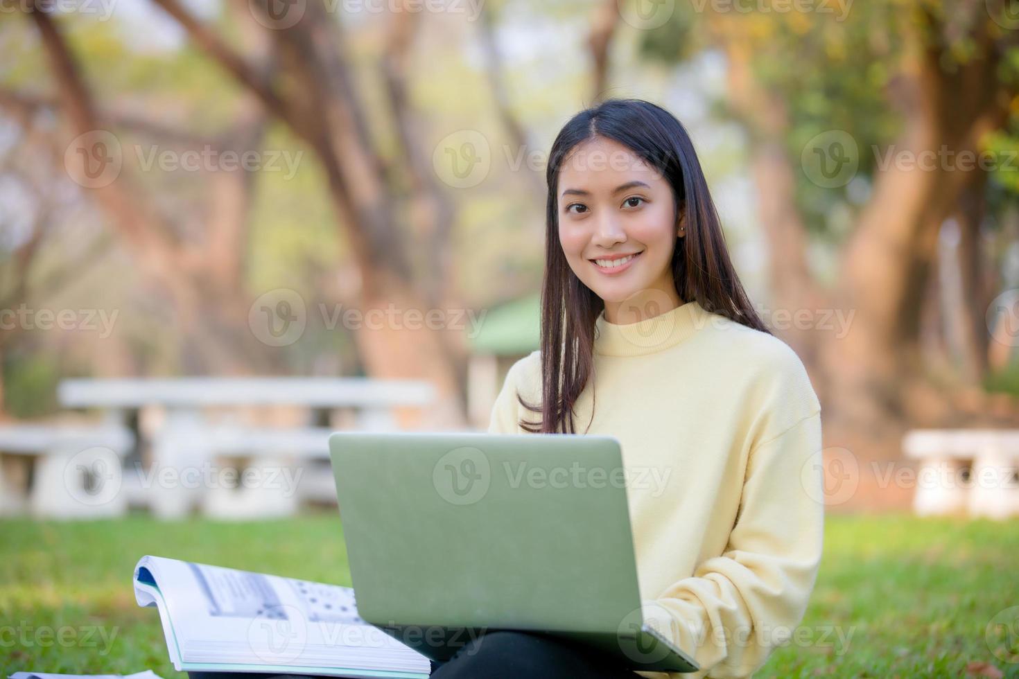 Asian women University Students smiling and sitting on the green grass  Working and reading Outside Together in a park photo