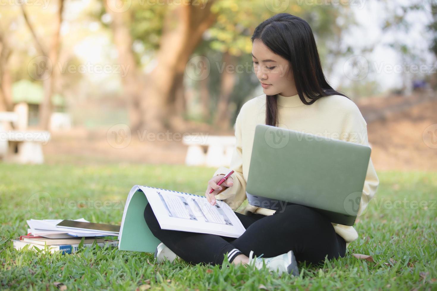 Mujeres asiáticas estudiantes universitarios sonriendo y sentados en la hierba verde trabajando y leyendo juntos afuera en un parque foto