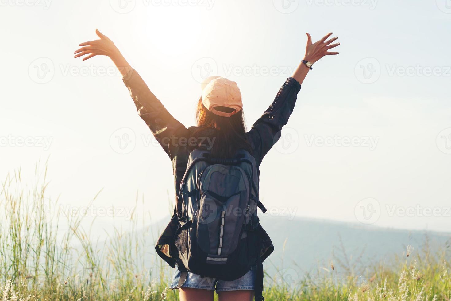 Freedom traveler woman standing with raised arms and enjoying a beautiful nature and cheering young woman backpacker at sunrise seaside mountain peak photo