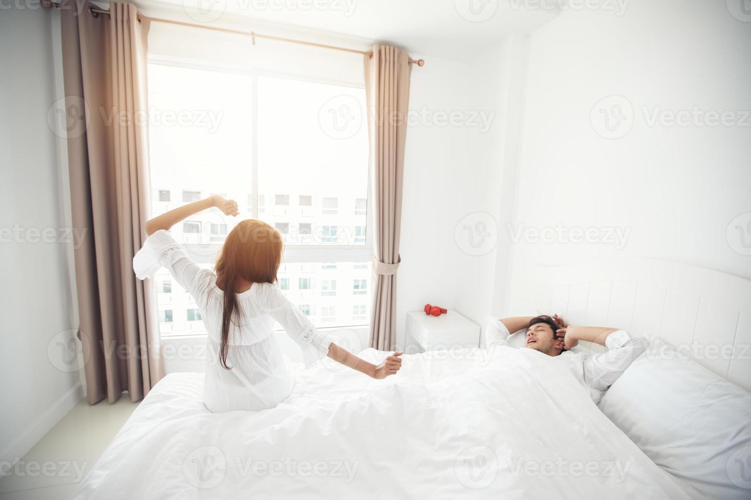 Amante de las parejas que se despierta en su cama completamente descansada y abre las cortinas por la mañana para que entre aire fresco. foto