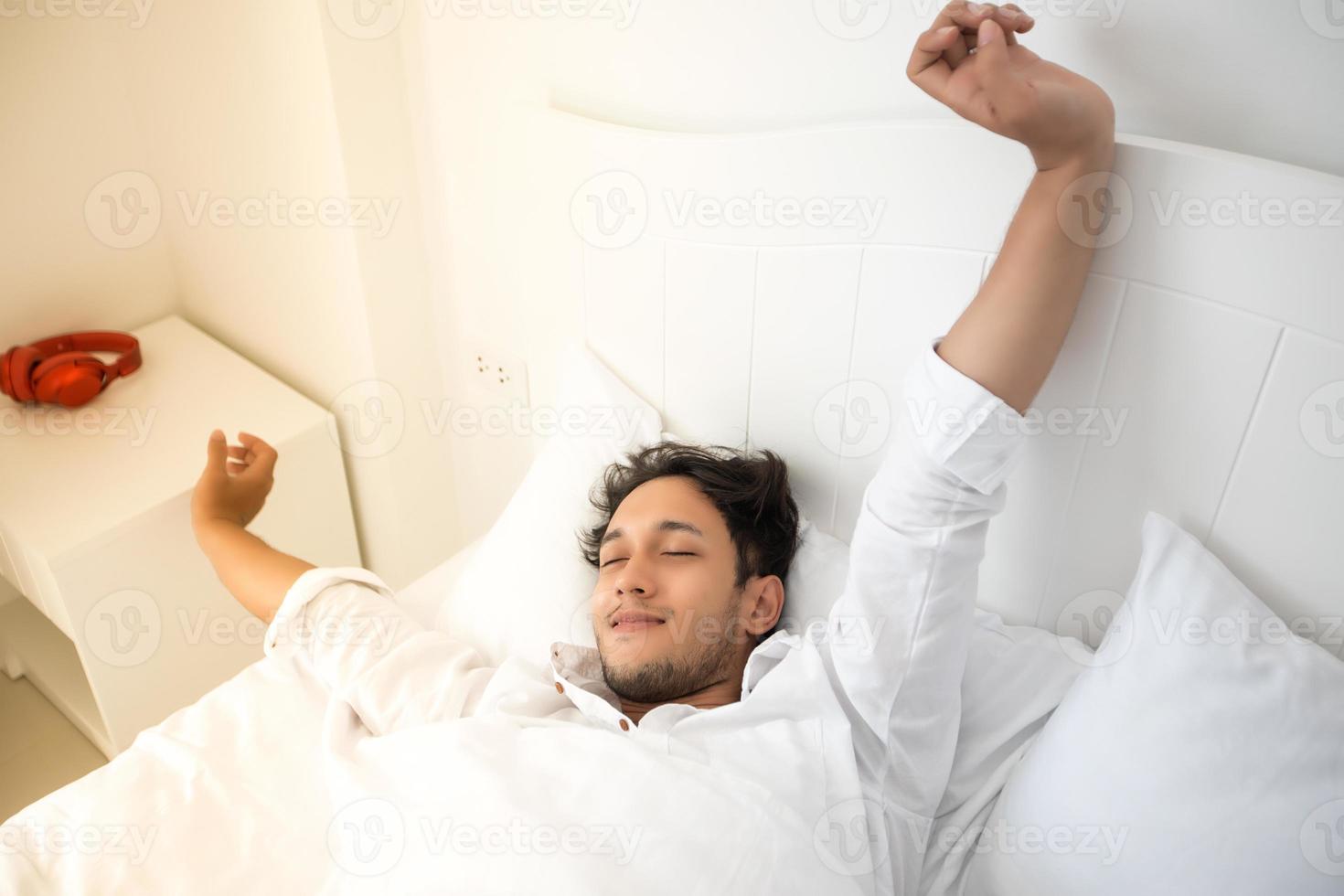 un hombre se despierta en su cama completamente descansado y abre las cortinas por la mañana para tomar aire fresco. foto