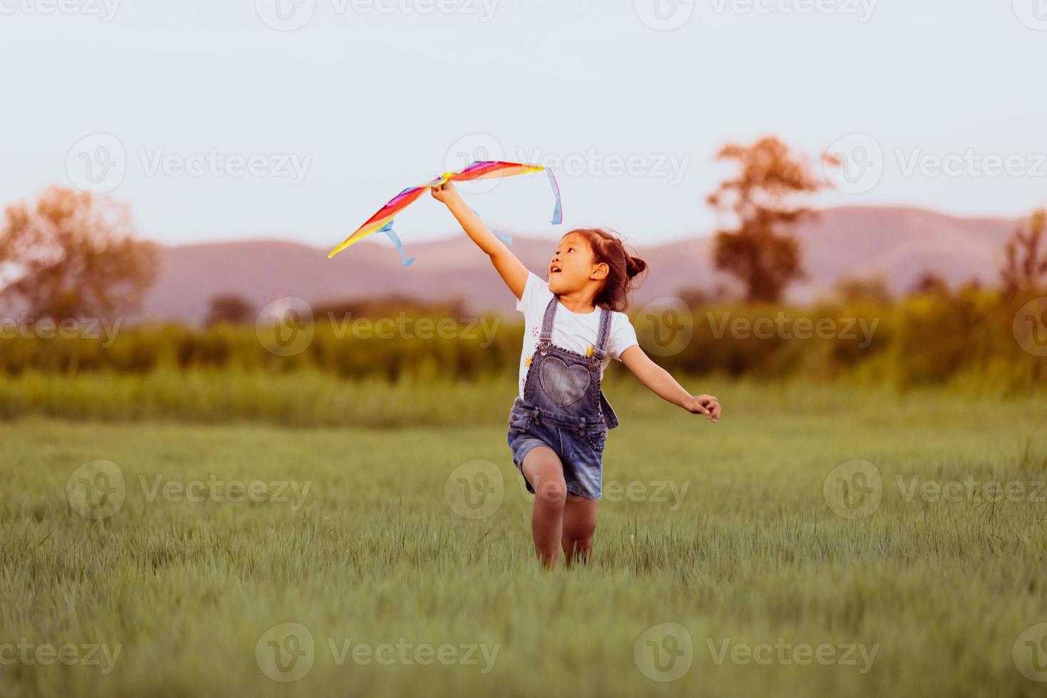 Niña asiática y padre con una cometa corriendo y feliz en la pradera en verano en la naturaleza foto