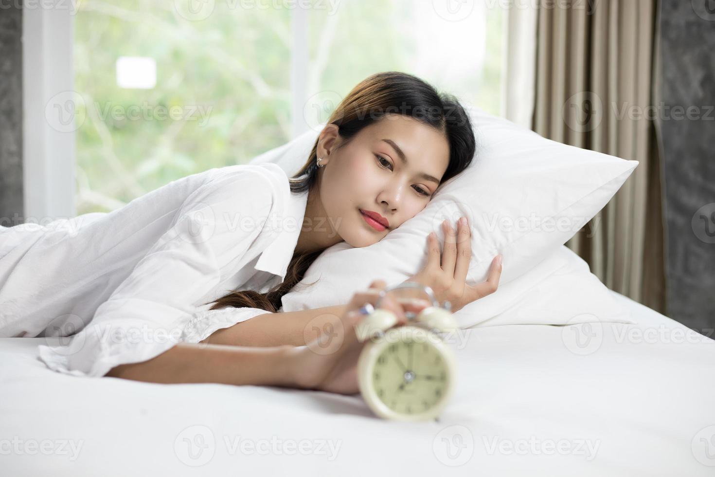 Mujer asiática feliz despertando y apagando el despertador teniendo un buen día foto