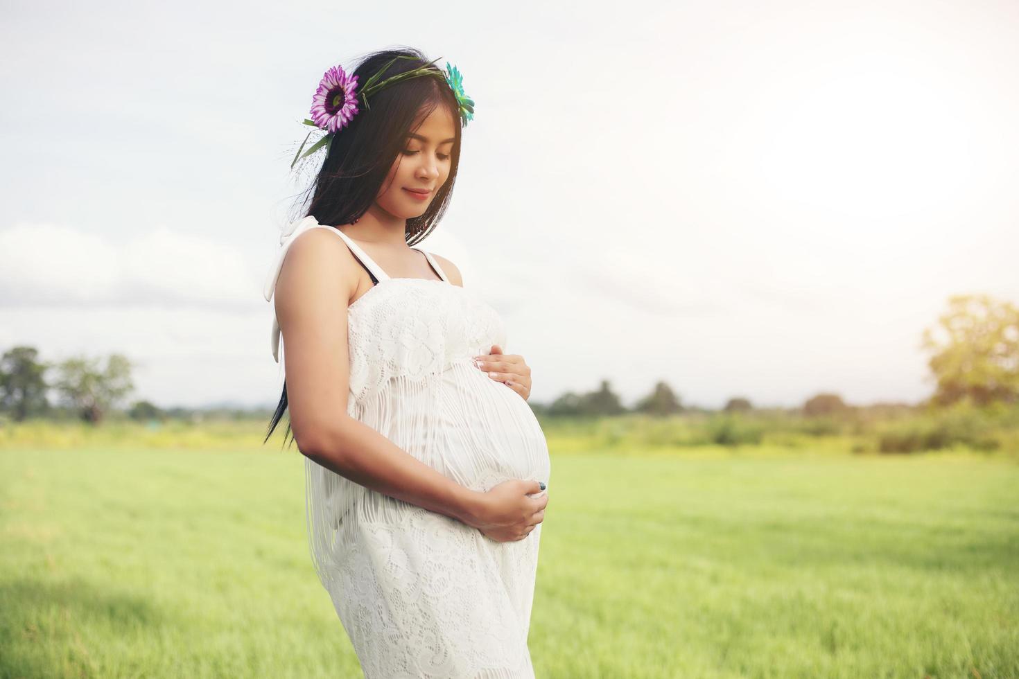 Feliz y orgullosa mujer asiática embarazada mirando su vientre en un parque al amanecer. foto