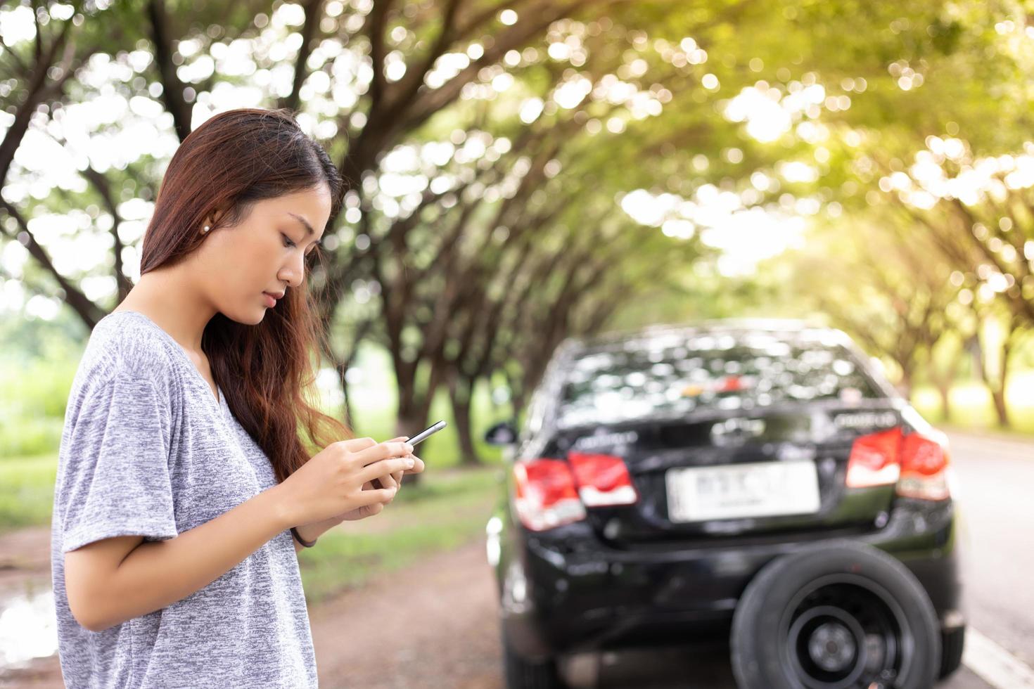 Mujer asiática con teléfono móvil mientras mira y estresado hombre sentado después de una avería de coche en la calle foto