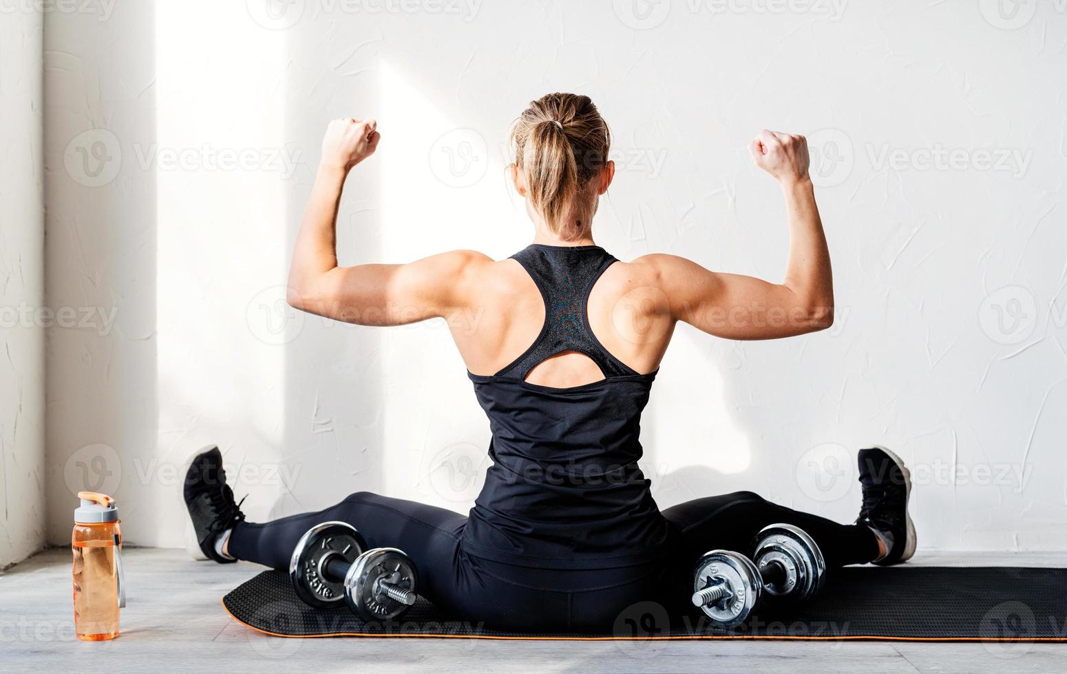 Vista trasera de la joven mujer rubia trabajando con pesas mostrando sus músculos de la espalda y los brazos foto