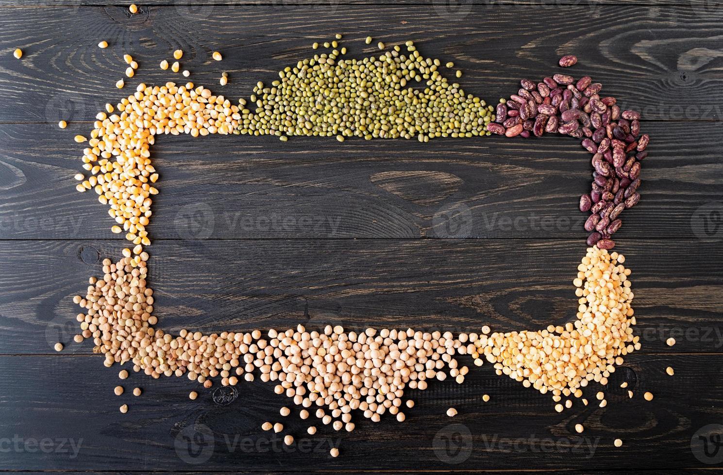 Various dried legumes forming a frame top view flat lay on black wooden background photo