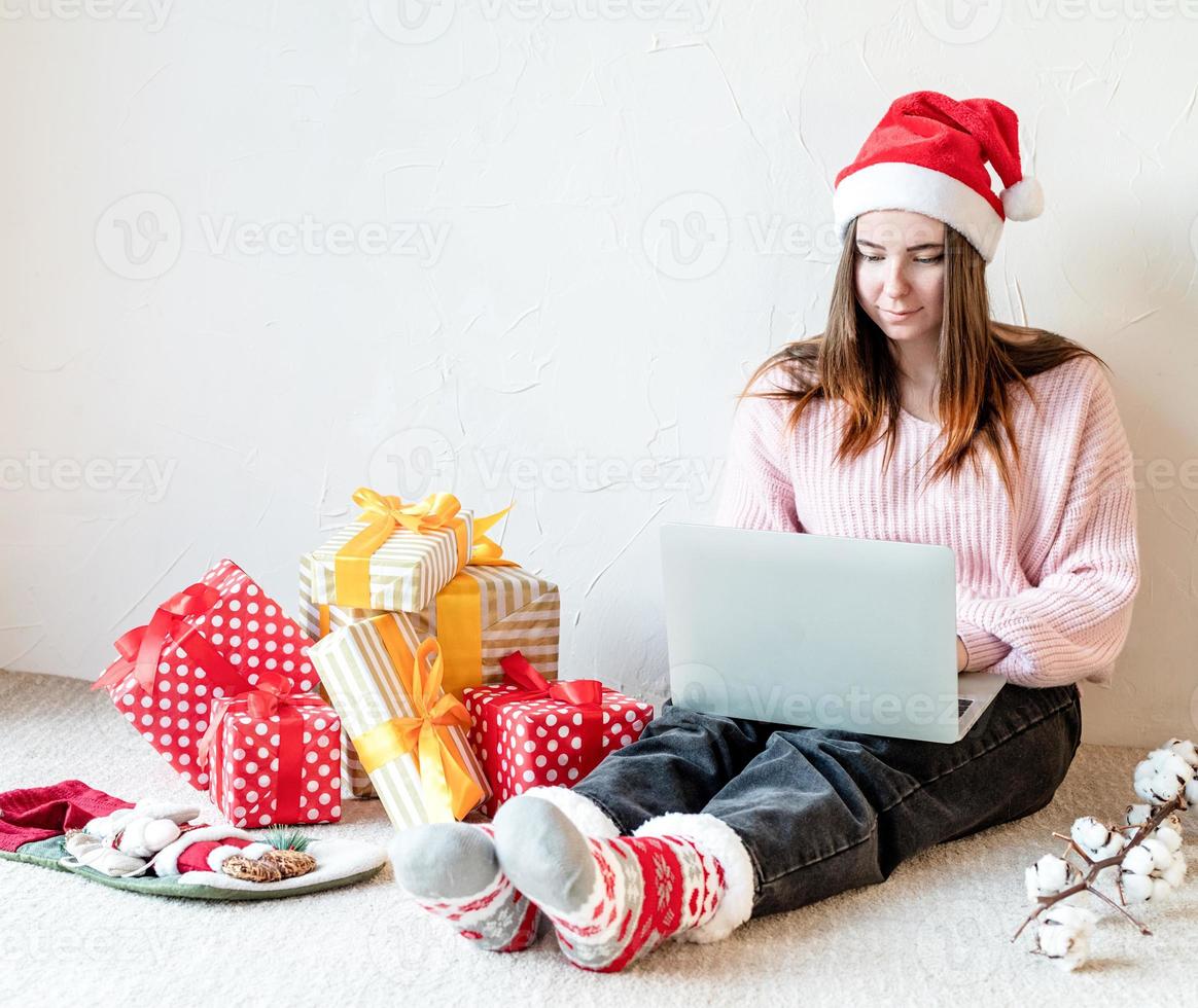 Mujer joven con gorro de Papá Noel de compras online rodeado de regalos foto