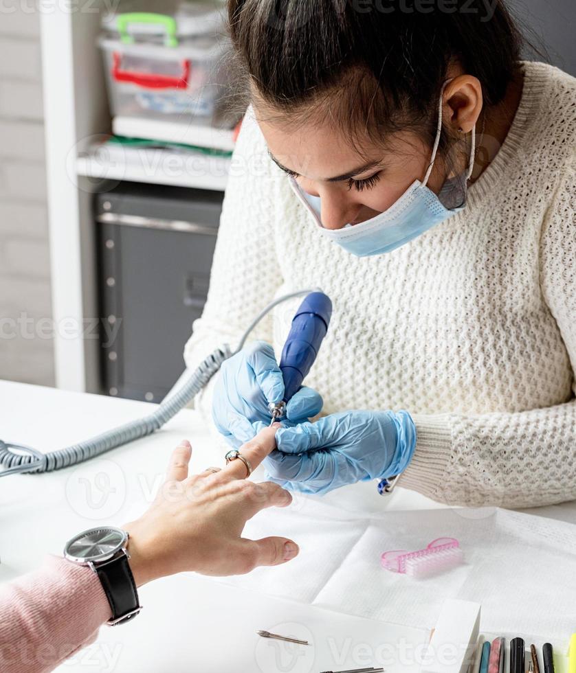 Manicure master using an electric machine to remove the nail polish during manicure in the salon photo