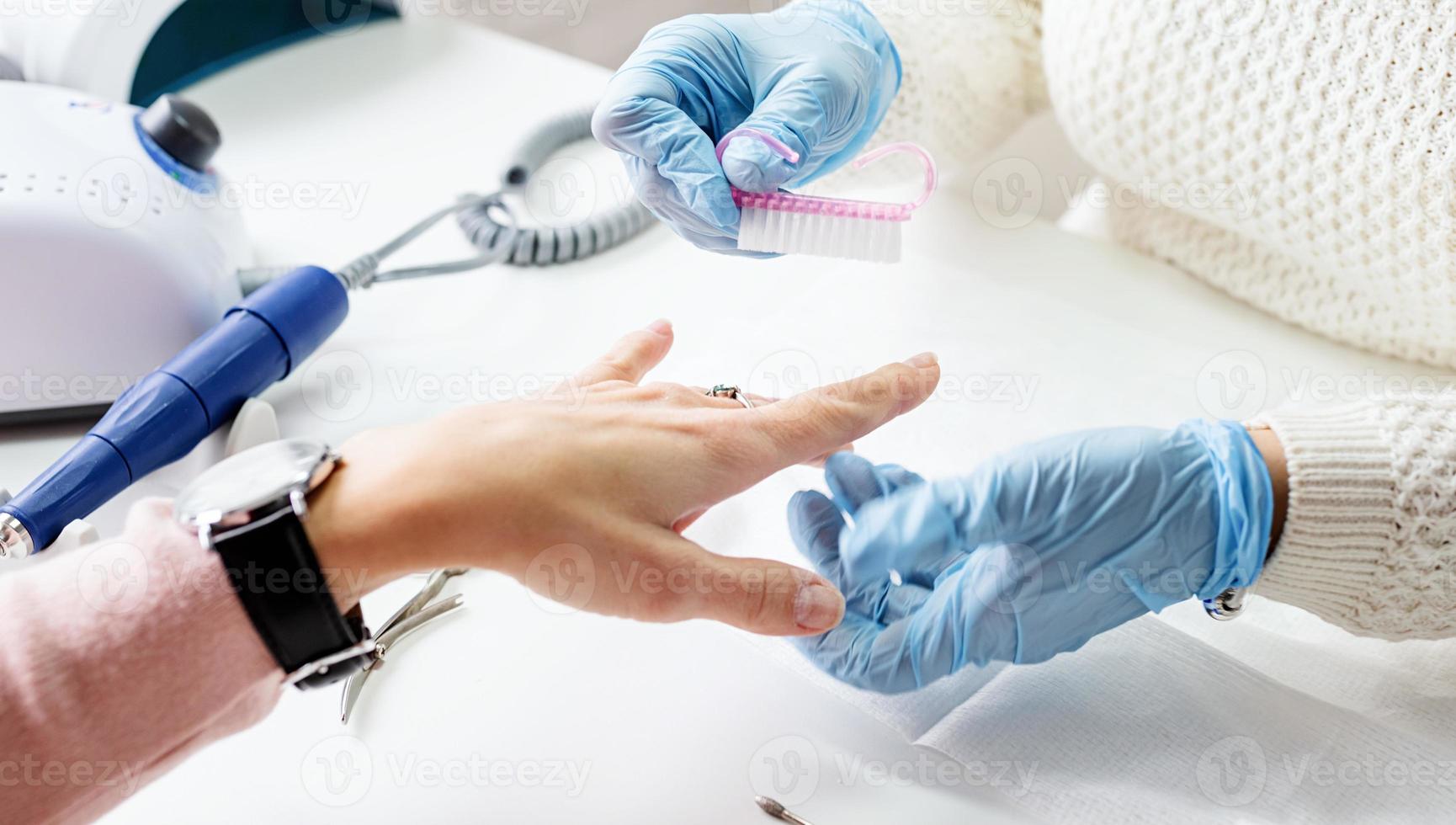 maestro de manicura usando un cepillo para limpiar el polvo después de quitar el esmalte en gel foto