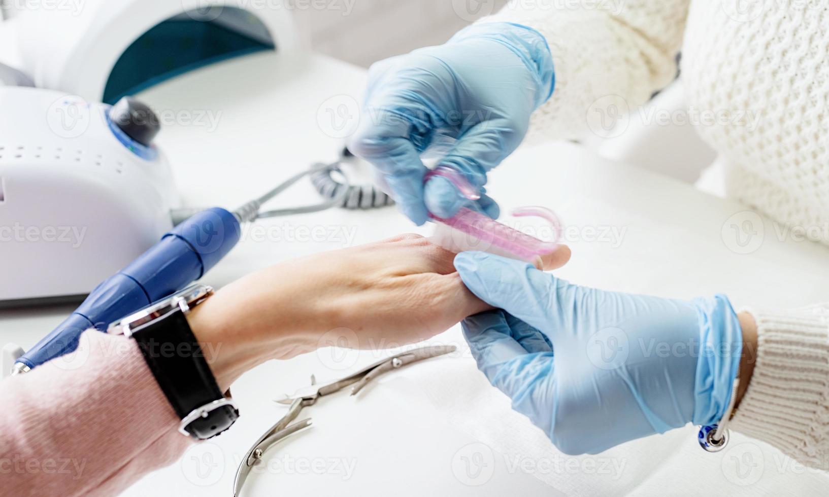 maestro de manicura usando un cepillo para limpiar el polvo después de quitar el esmalte en gel foto