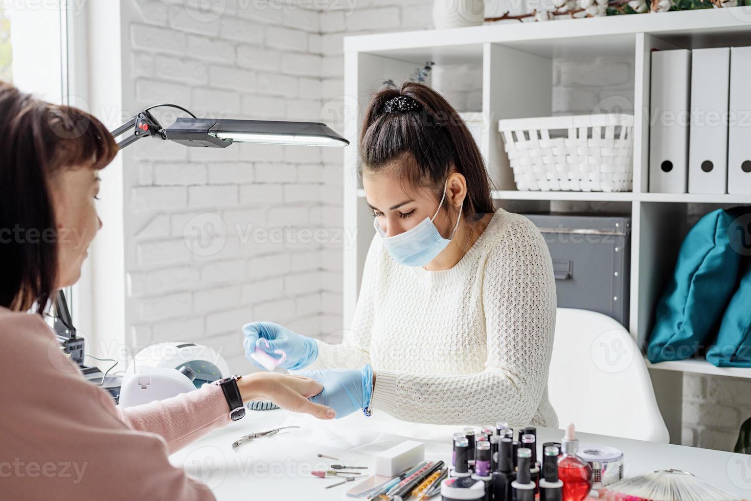 Manicure master using an electric machine to remove the nail polish during manicure in the salon photo