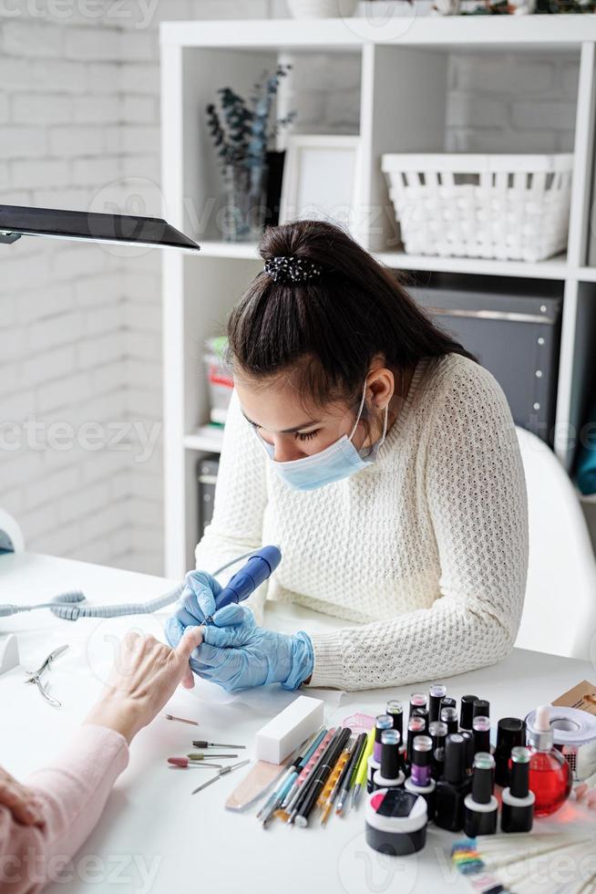 maestro de manicura usando una máquina eléctrica para quitar el esmalte de uñas durante la manicura en el salón foto